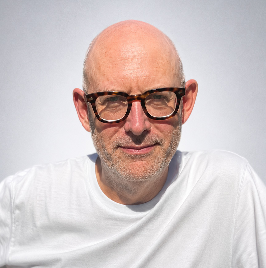Kevin Chesters portrait wearing glasses and a white T-shirt for the About Kevin section